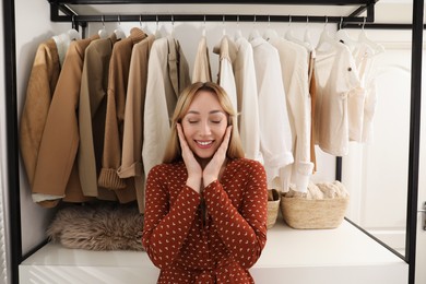 Photo of Happy young woman near rack with different clothes in dressing room