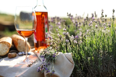 Composition with glass of wine on wicker table in lavender field. Space for text