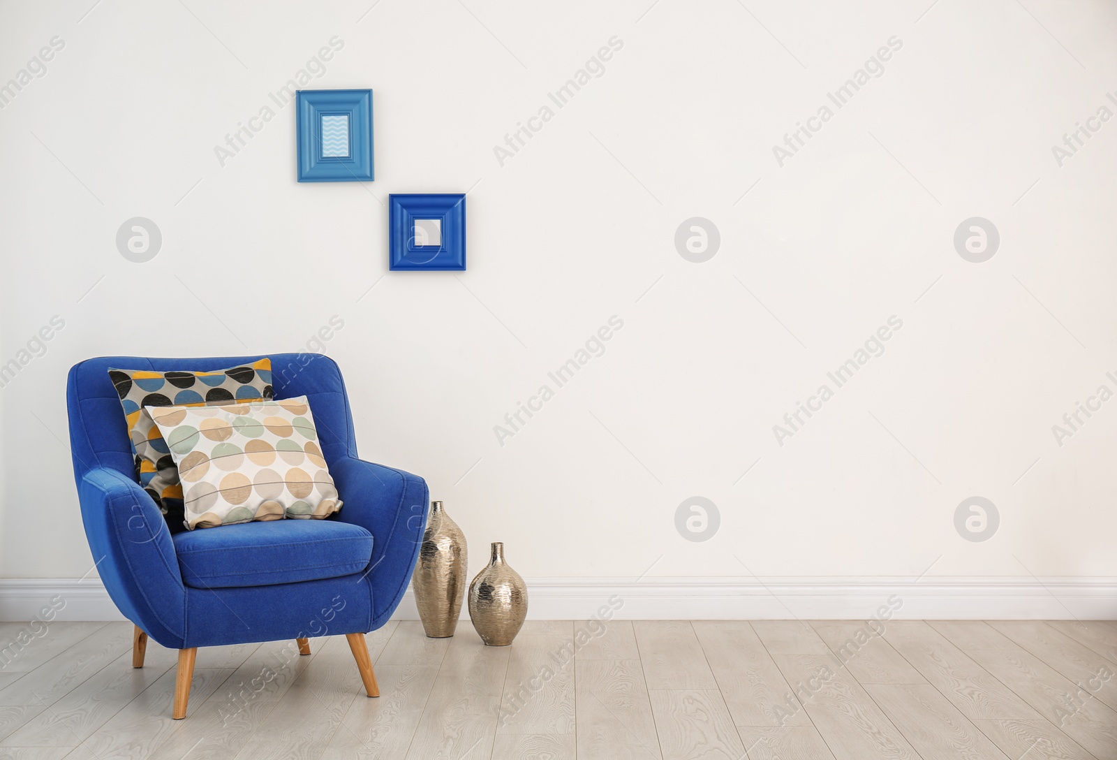 Photo of Armchair with different pillows near white wall in room