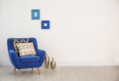 Armchair with different pillows near white wall in room