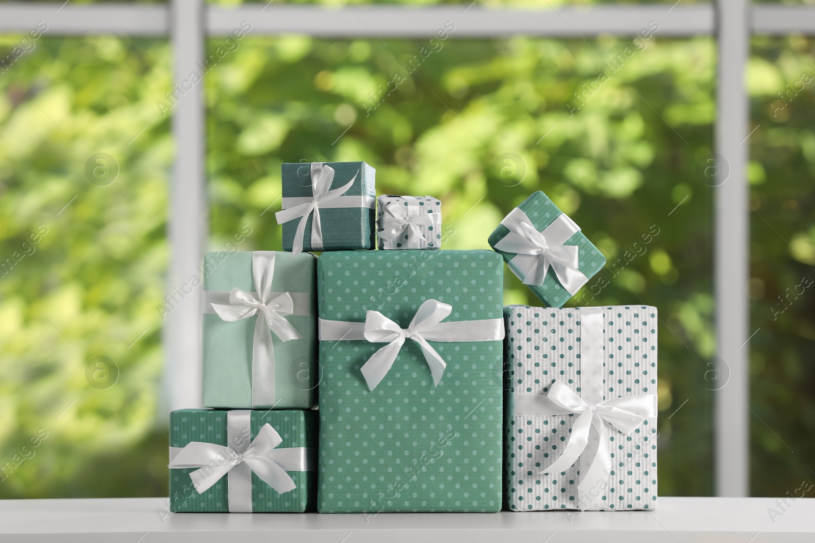 Photo of Many beautifully wrapped gift boxes on white table  near window