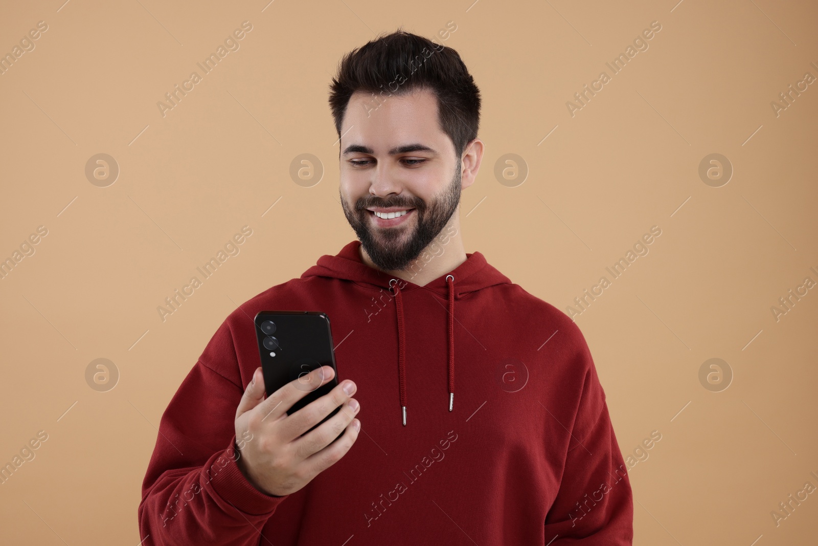 Photo of Happy young man using smartphone on beige background