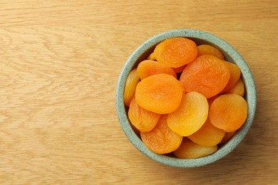 Bowl of tasty apricots on wooden table, top view and space for text. Dried fruits