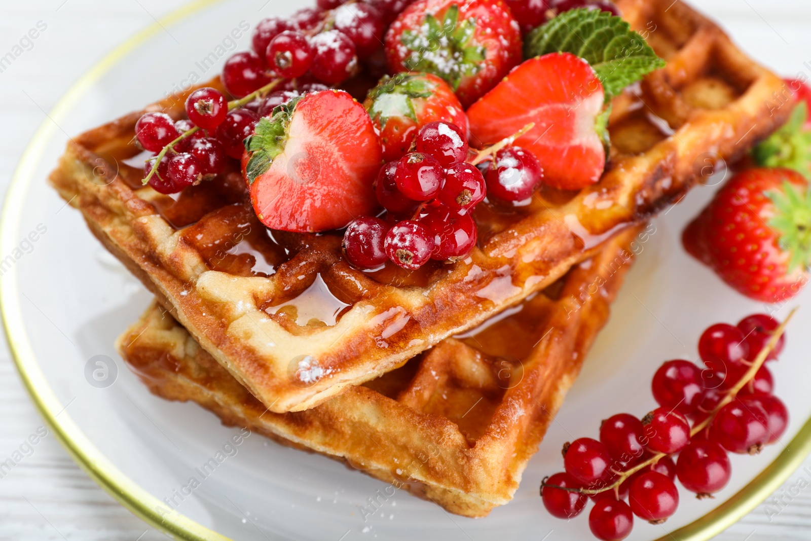 Photo of Delicious Belgian waffles with berries and honey on plate, closeup