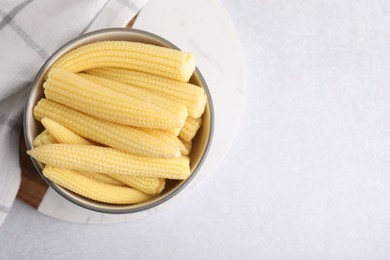 Photo of Tasty fresh yellow baby corns in bowl on white table, top view. Space for text