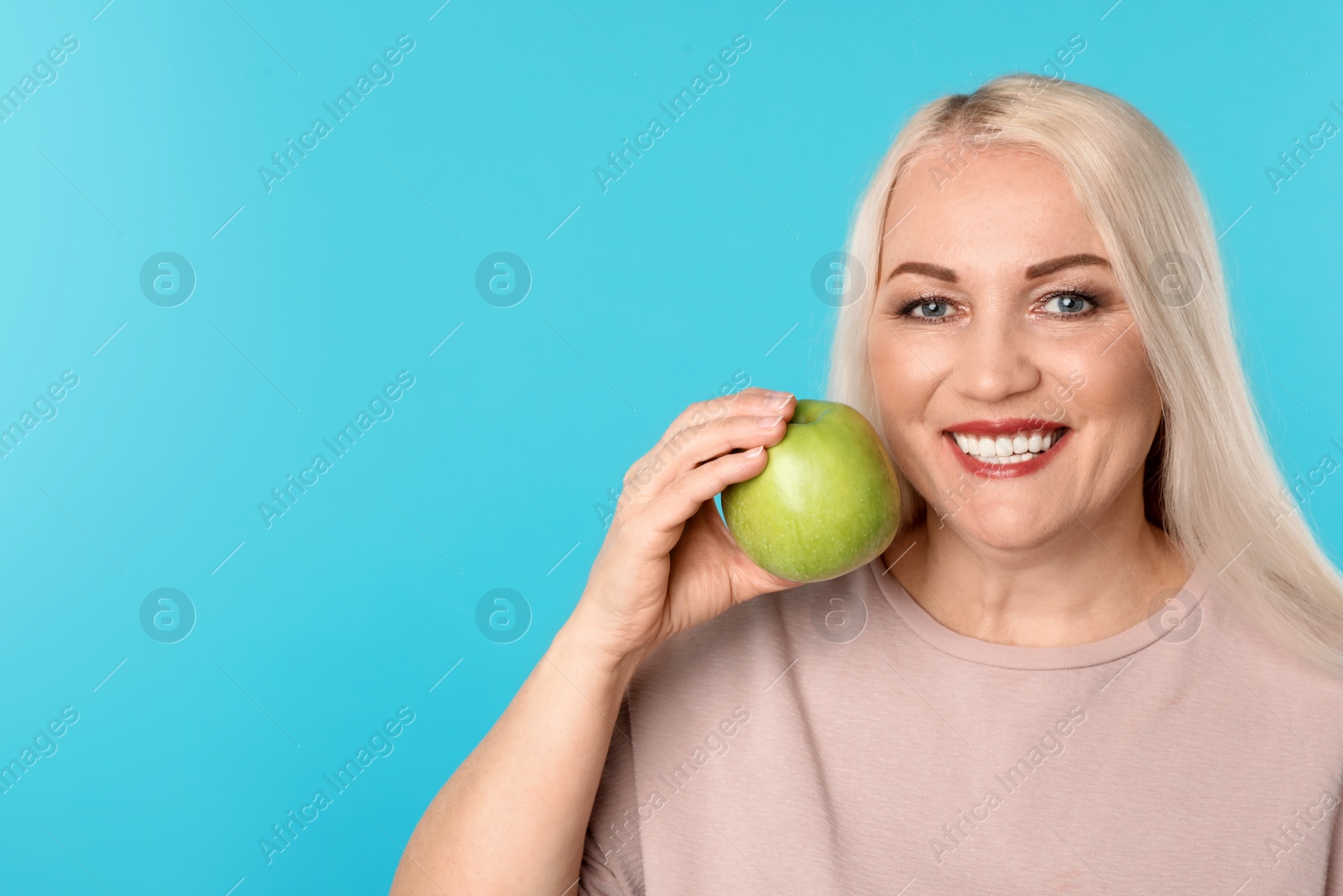 Photo of Smiling woman with perfect teeth and green apple on color background. Space for text