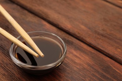 Bowl with soy sauce and chopsticks on wooden table, closeup. Space for text