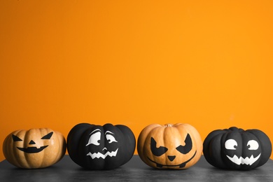 Photo of Pumpkins with scary faces on table against color background, space for text. Halloween decor