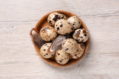 Photo of Fresh quail eggs and feathers on white wooden table, top view