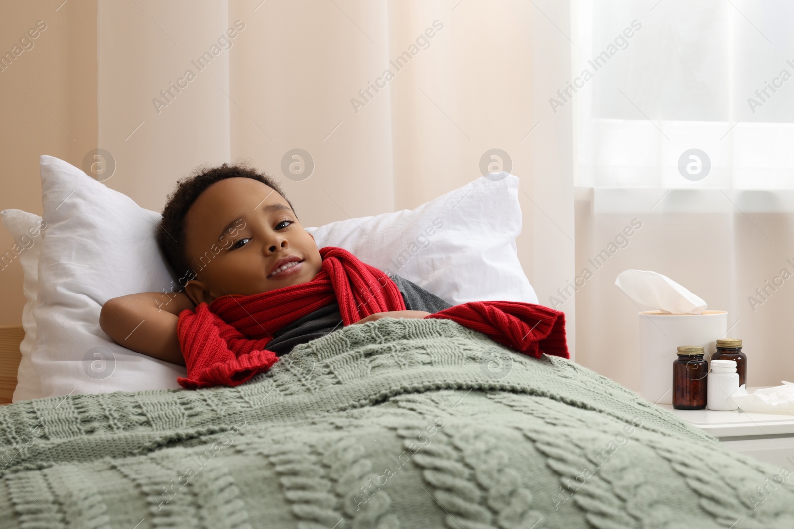 Photo of African American boy with scarf lying in bed indoors. Cold symptoms