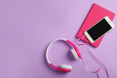 Photo of Modern headphones, phone and notebook on color background, flat lay. Space for text