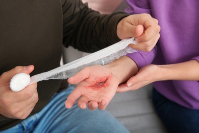 Photo of Young man applying bandage on woman's injured hand at home, closeup. First aid