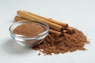 Photo of Cinnamon powder and sticks on white wooden table