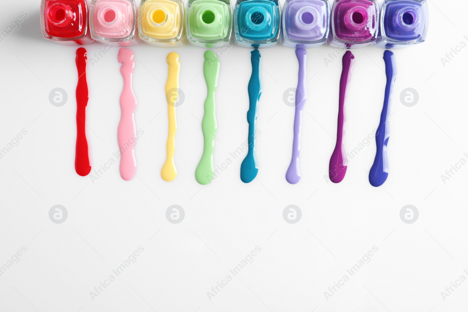 Photo of Spilled colorful nail polishes and bottles on white background, top view