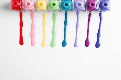 Spilled colorful nail polishes and bottles on white background, top view