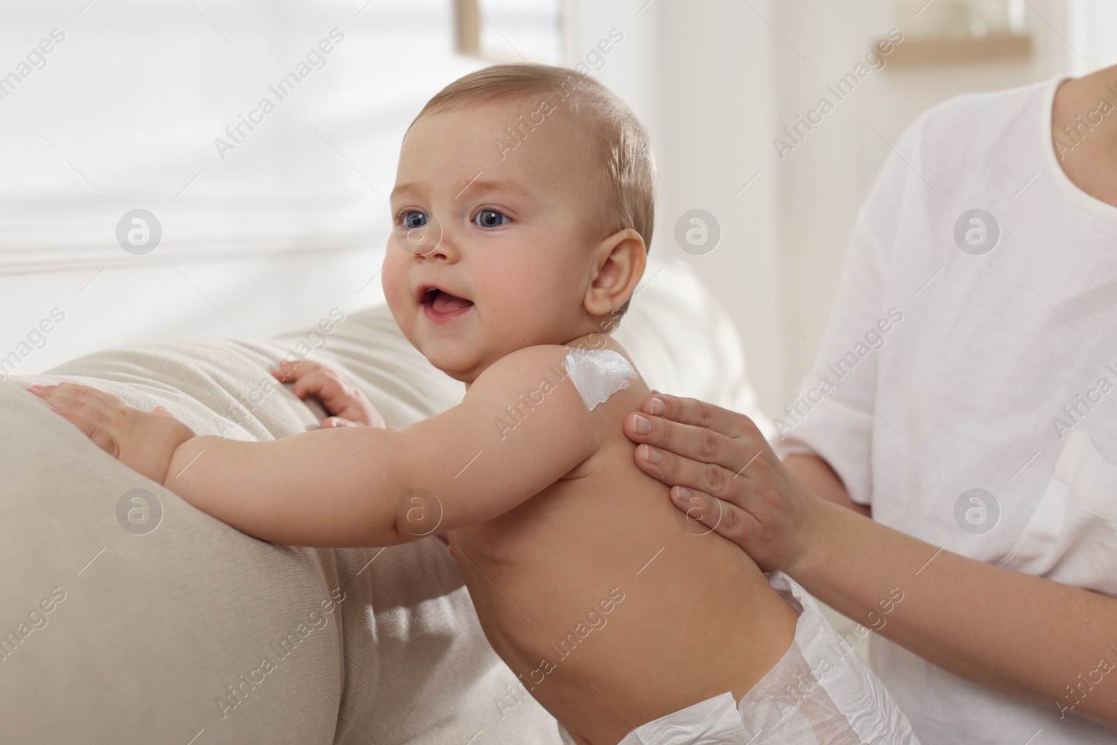 Photo of Mother applying body cream on her little baby at home, closeup