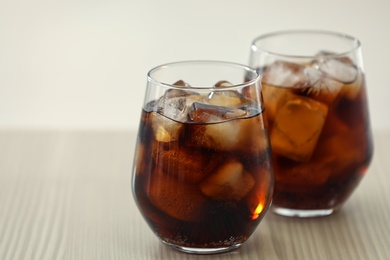 Glasses of cola with ice on table against blurred background