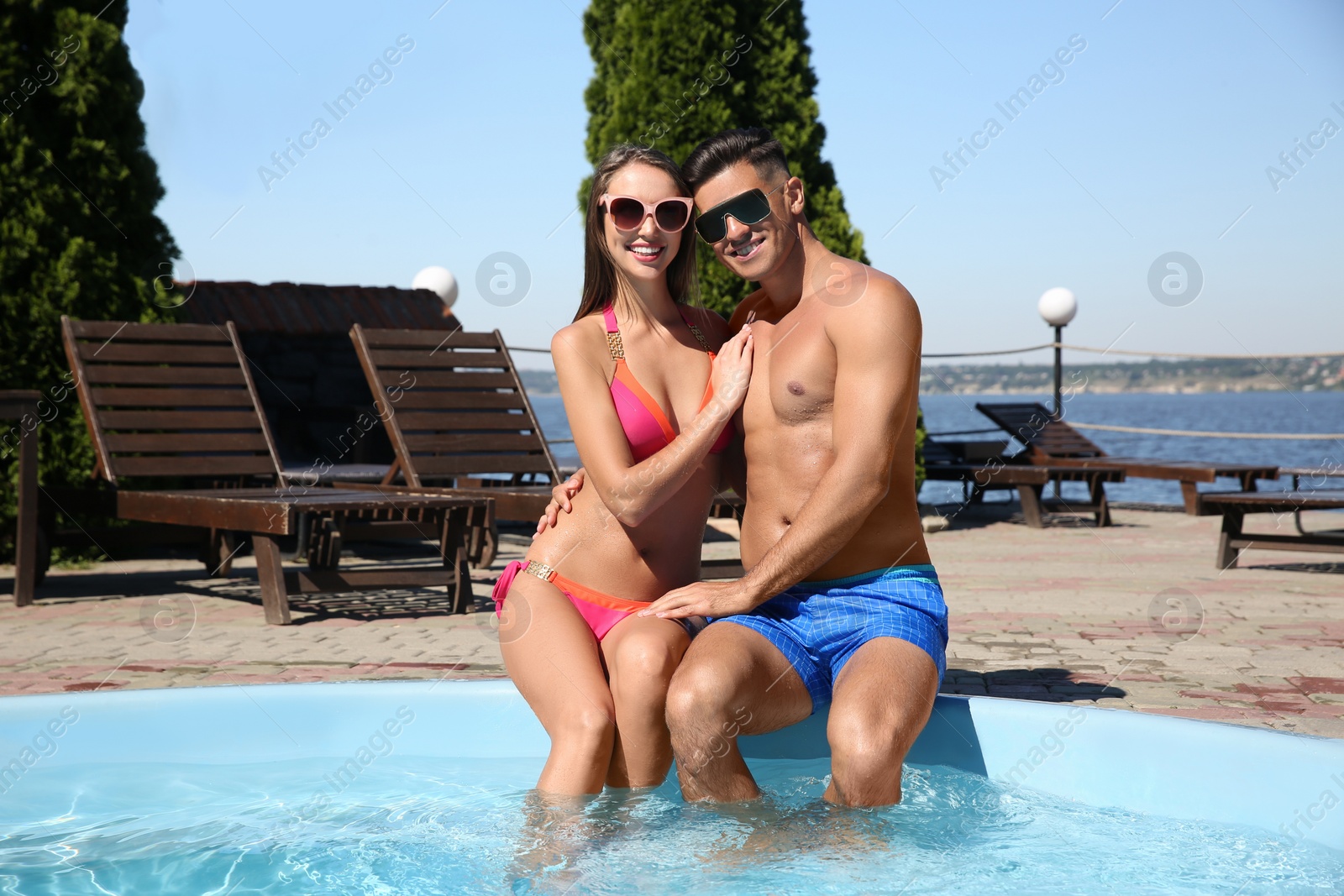 Photo of Happy couple sitting at poolside on sunny summer day