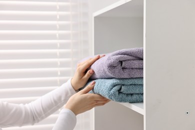 Woman stacking clean towels on shelf indoors, closeup