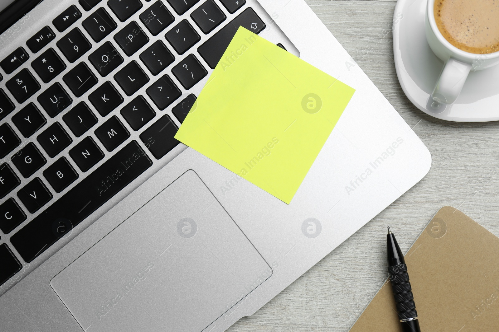 Photo of Laptop with blank sticky note, pen and cup of coffee on white wooden table, flat lay. Space for text