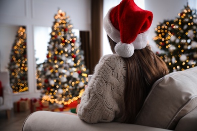 Photo of Beautiful young woman wearing Santa hat in room decorated for Christmas, back view