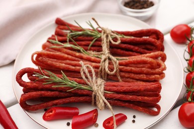 Photo of Bundles of delicious kabanosy with rosemary, peppercorn, chilli and tomatoes on white wooden table, closeup