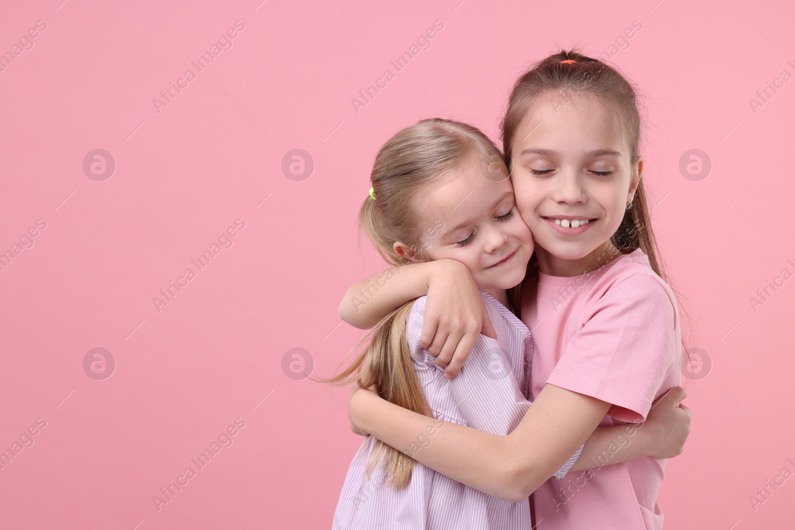Photo of Portrait of cute little sisters on pink background, space for text