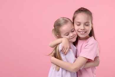 Portrait of cute little sisters on pink background, space for text