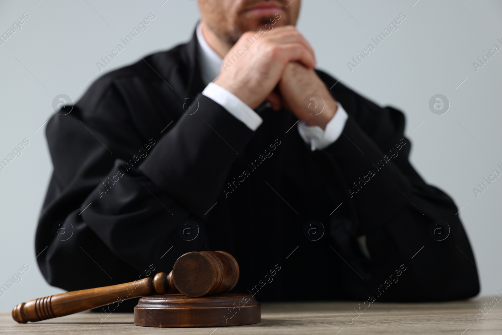 Photo of Judge with gavel sitting at wooden table against light grey background, closeup