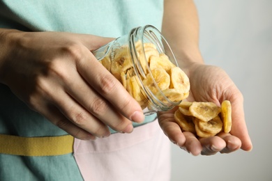 Photo of Woman pouring sweet banana slices from jar to hand on light background, closeup. Dried fruit as healthy snack