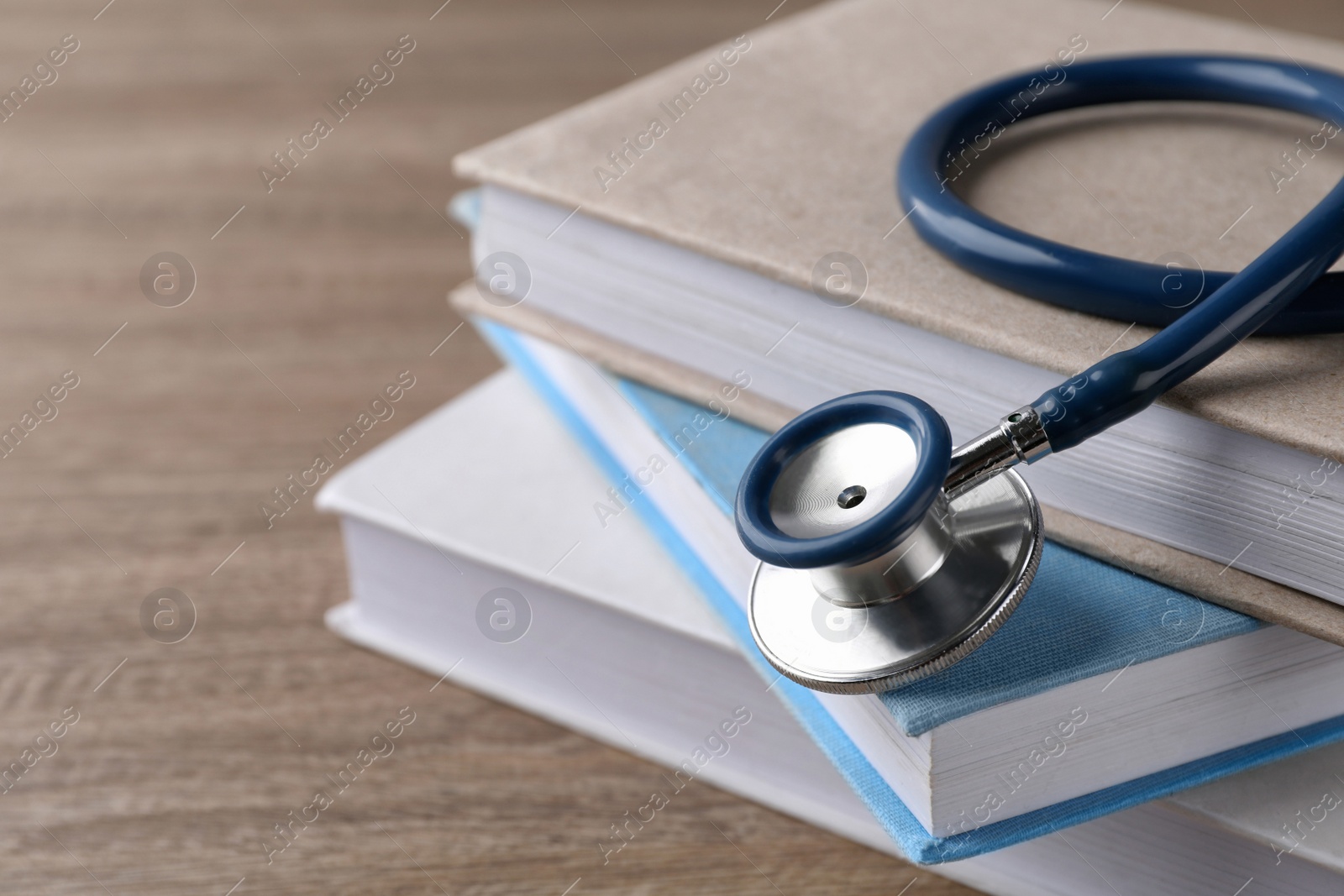 Photo of Student textbooks and stethoscope on wooden table, closeup view with space for text Medical education