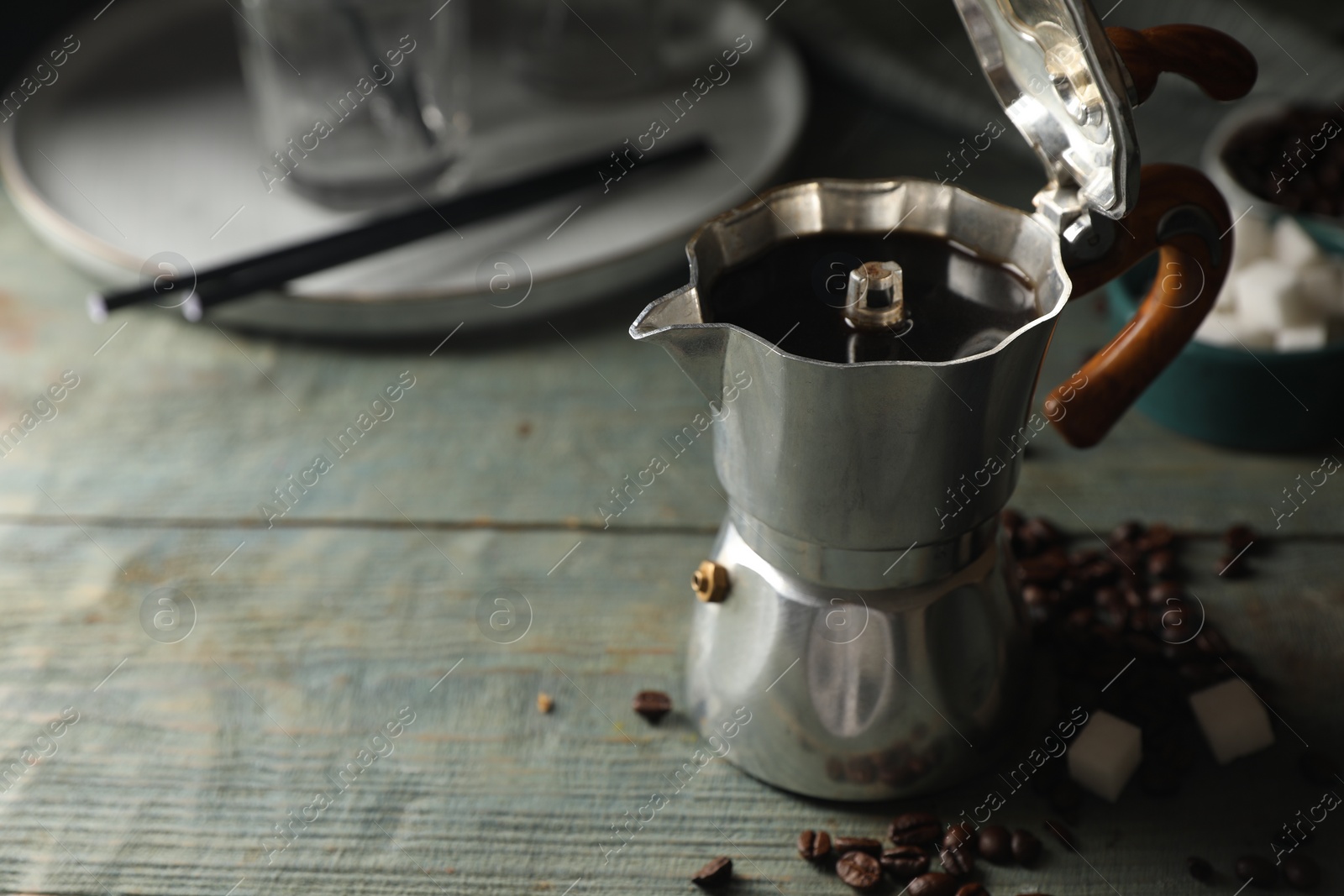 Photo of Brewed coffee in moka pot, beans and sugar cubes on rustic wooden table, space for text