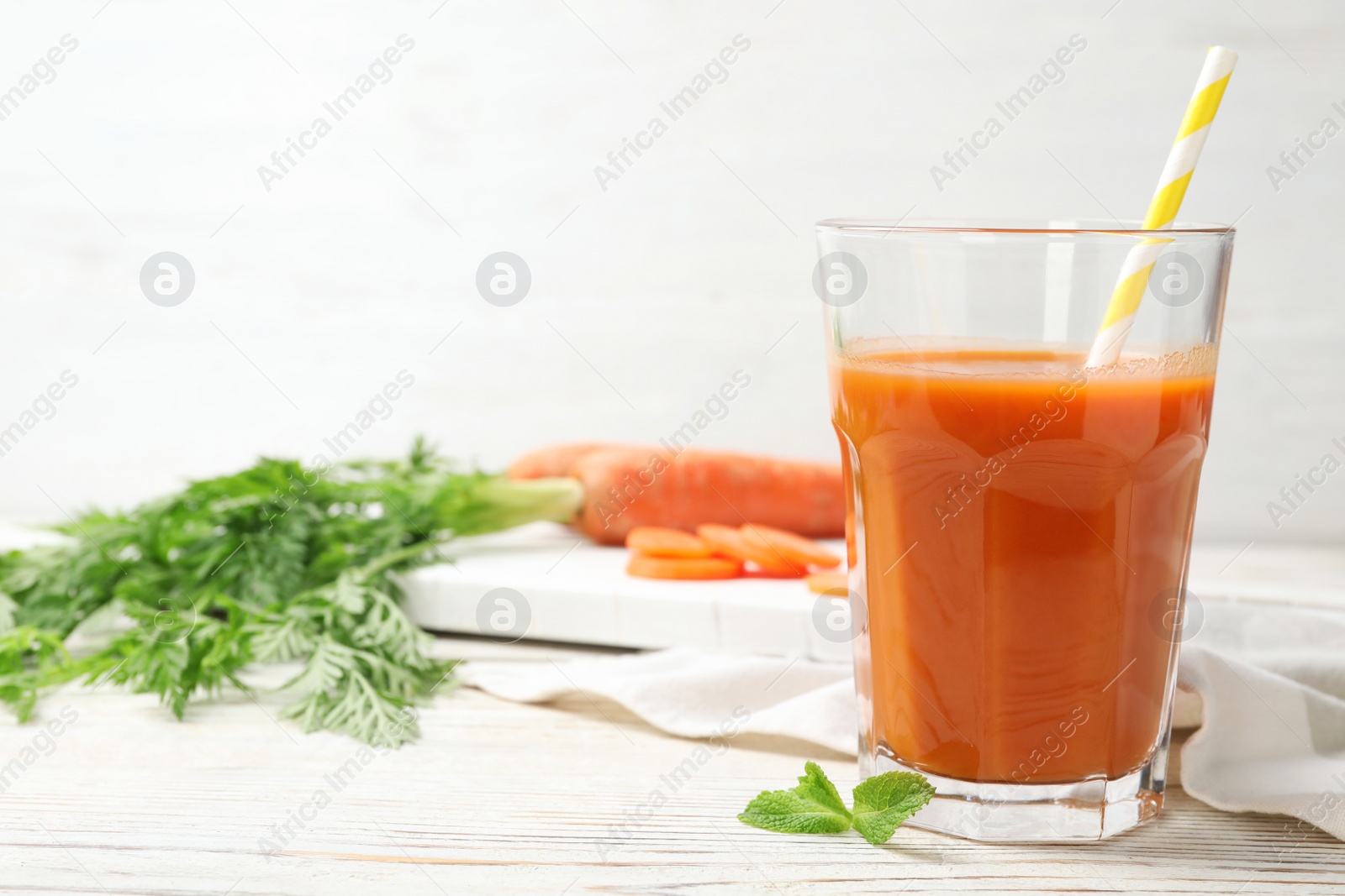 Photo of Glass of fresh carrot juice on white wooden table, space for text