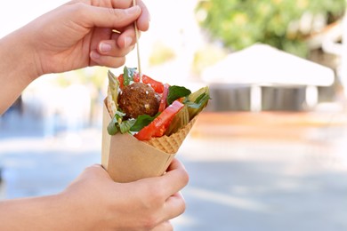 Photo of Woman eating wafer with falafel and vegetables outdoors, closeup. Space for text