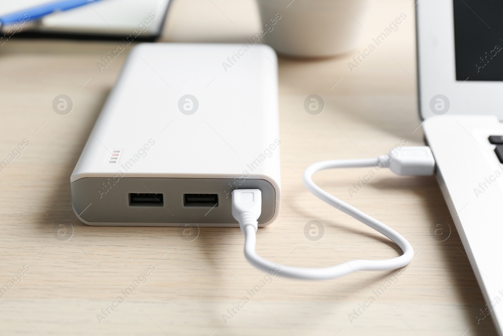 Photo of Charging modern laptop with power bank on wooden table, closeup