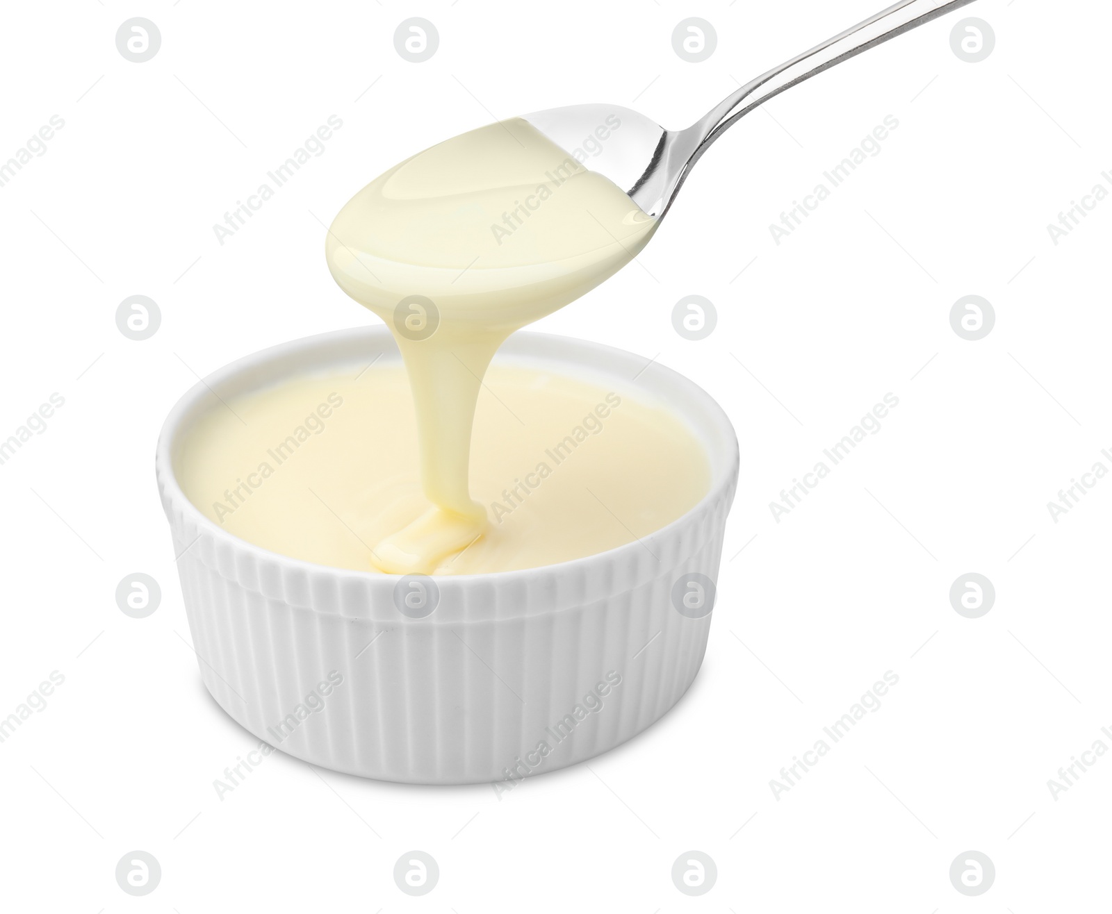 Photo of Condensed milk flowing down from spoon into bowl isolated on white