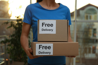 Photo of Courier holding parcels with stickers Free Delivery indoors, closeup