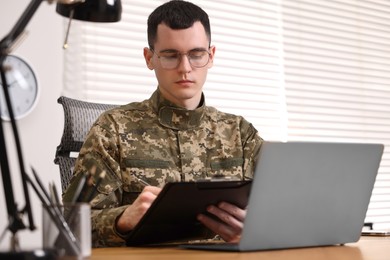 Photo of Military service. Young soldier working at table in office