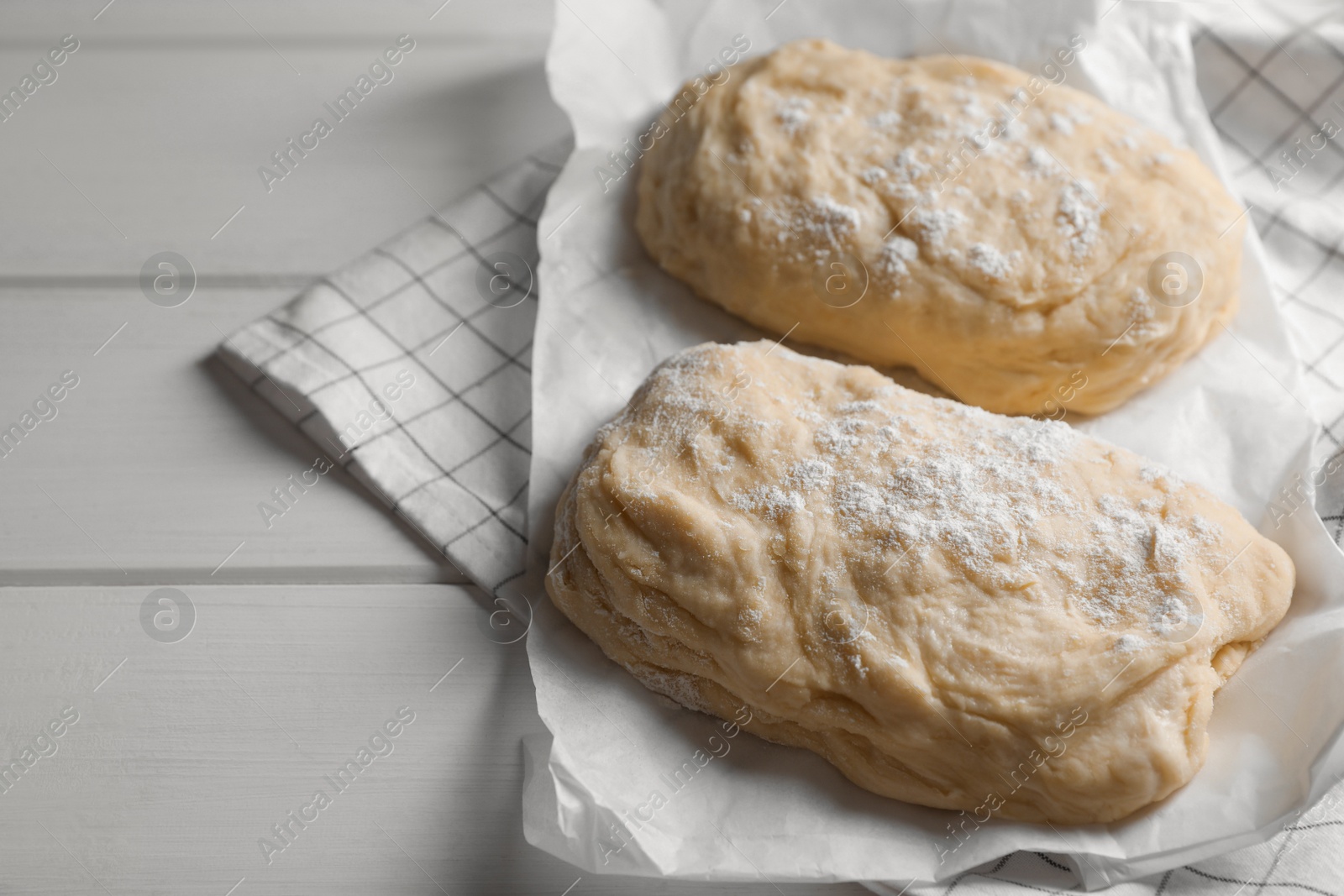 Photo of Raw dough and flour on white wooden table, space for text. Cooking ciabatta