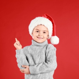 Photo of Cute little child wearing Santa hat on red background, space for text. Christmas holiday