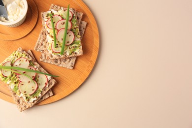 Fresh crunchy crispbreads with cream cheese, radish and green onion on beige table, top view. Space for text