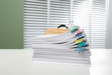 Photo of Stack of documents attached with colorful binder clips on white table in office