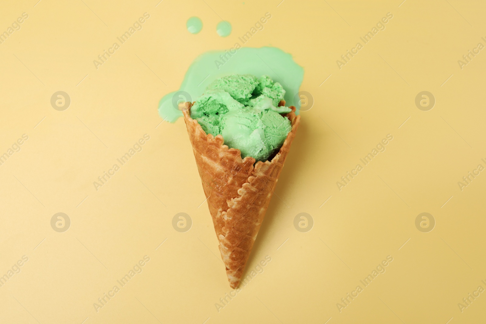 Photo of Melted ice cream in wafer cone on pale yellow background, top view