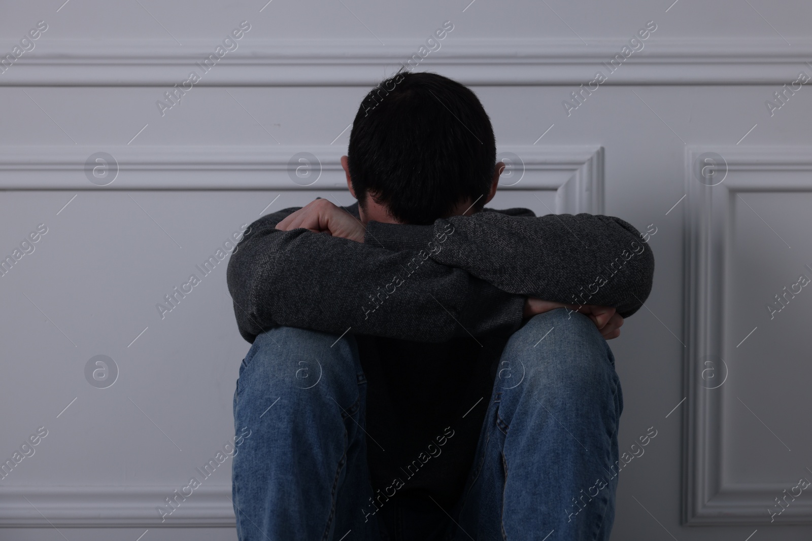 Photo of Sad man sitting near white wall indoors