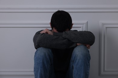 Photo of Sad man sitting near white wall indoors