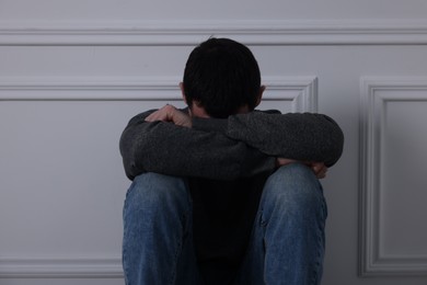 Sad man sitting near white wall indoors