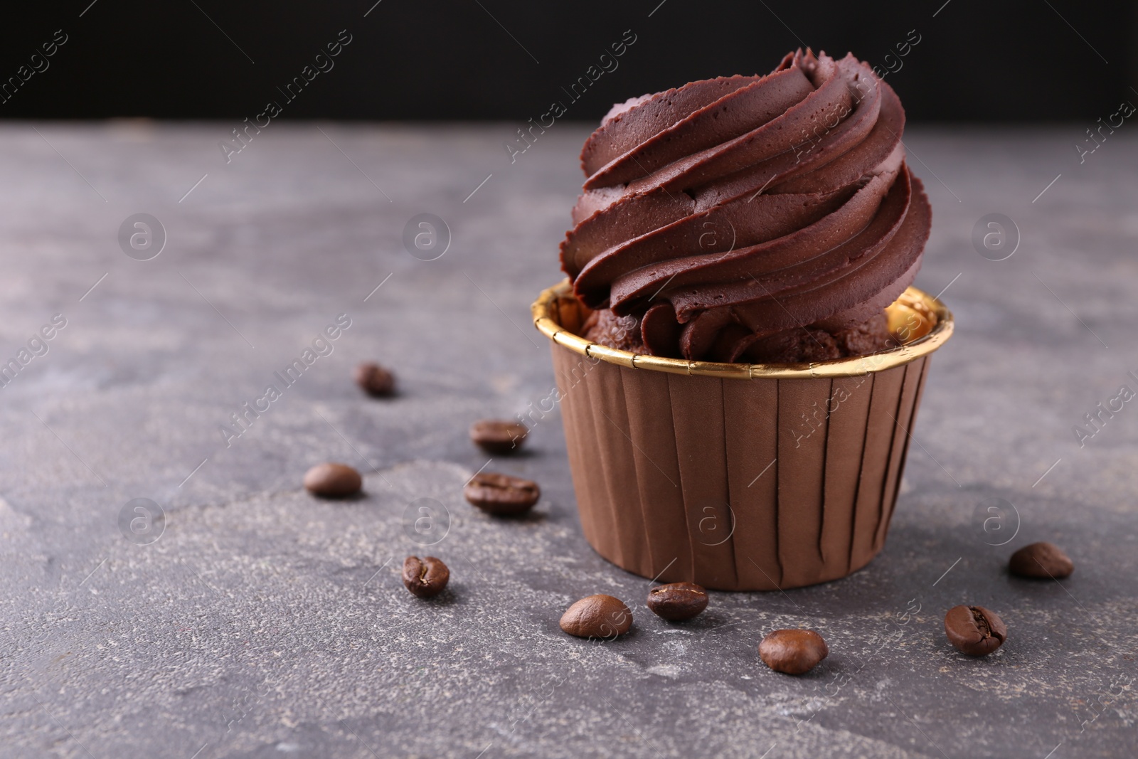 Photo of Delicious chocolate cupcake and coffee beans on grey textured table, closeup. Space for text