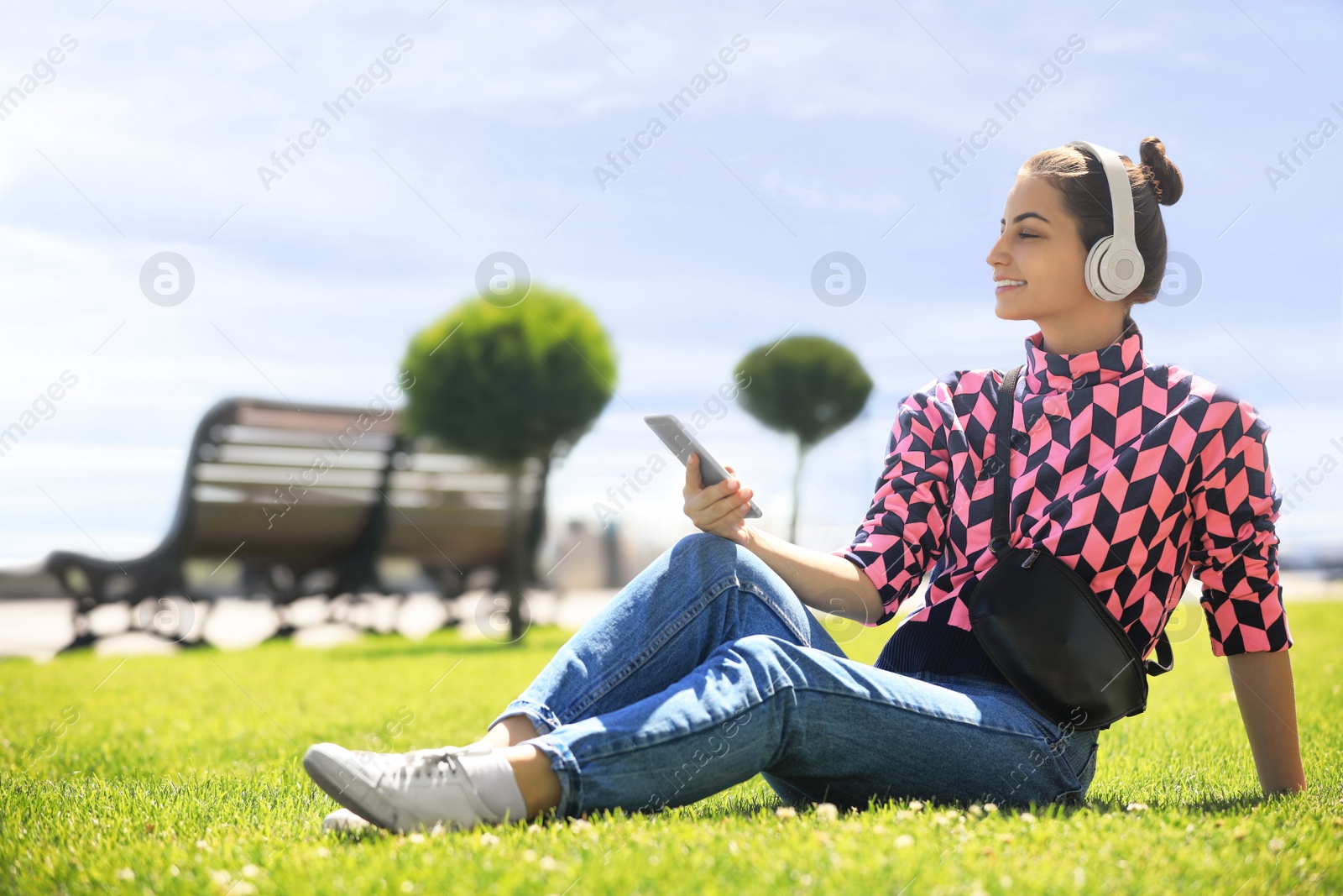 Photo of Young woman with headphones listening to music in park. Space for text