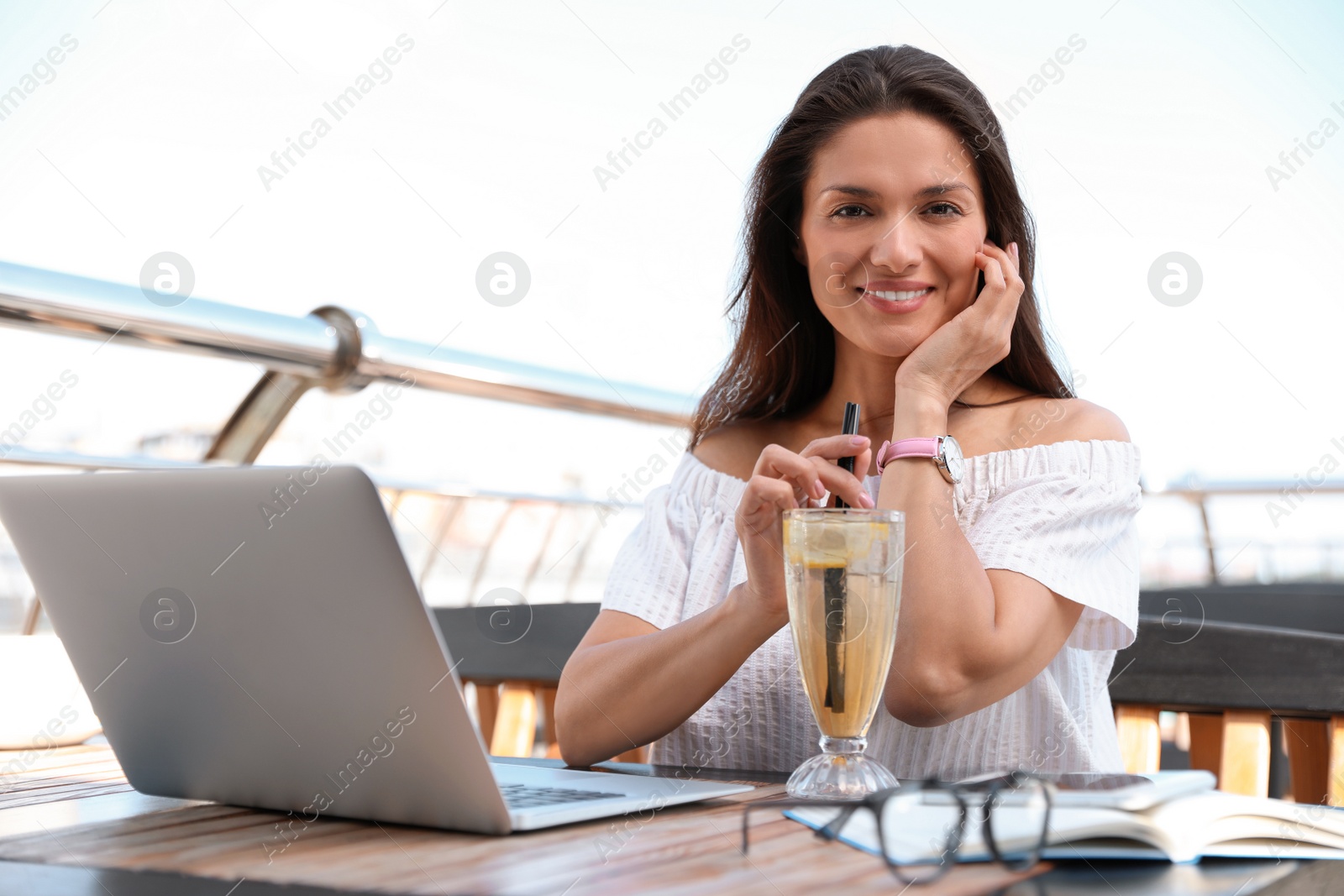 Photo of Beautiful woman with refreshing drink and laptop at outdoor cafe