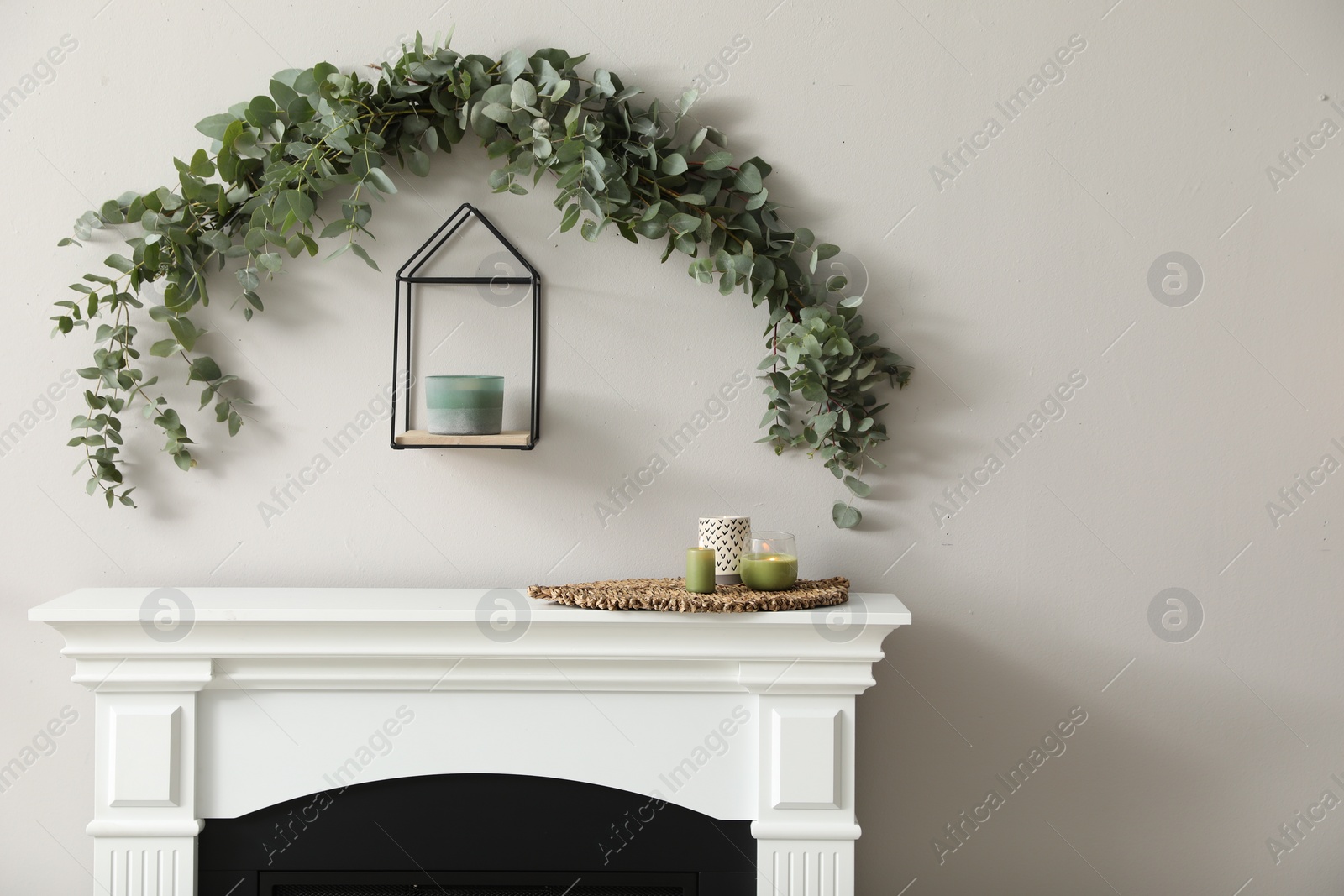 Photo of Beautiful garland made of eucalyptus branches and aromatic candle hanging above mantelpiece indoors